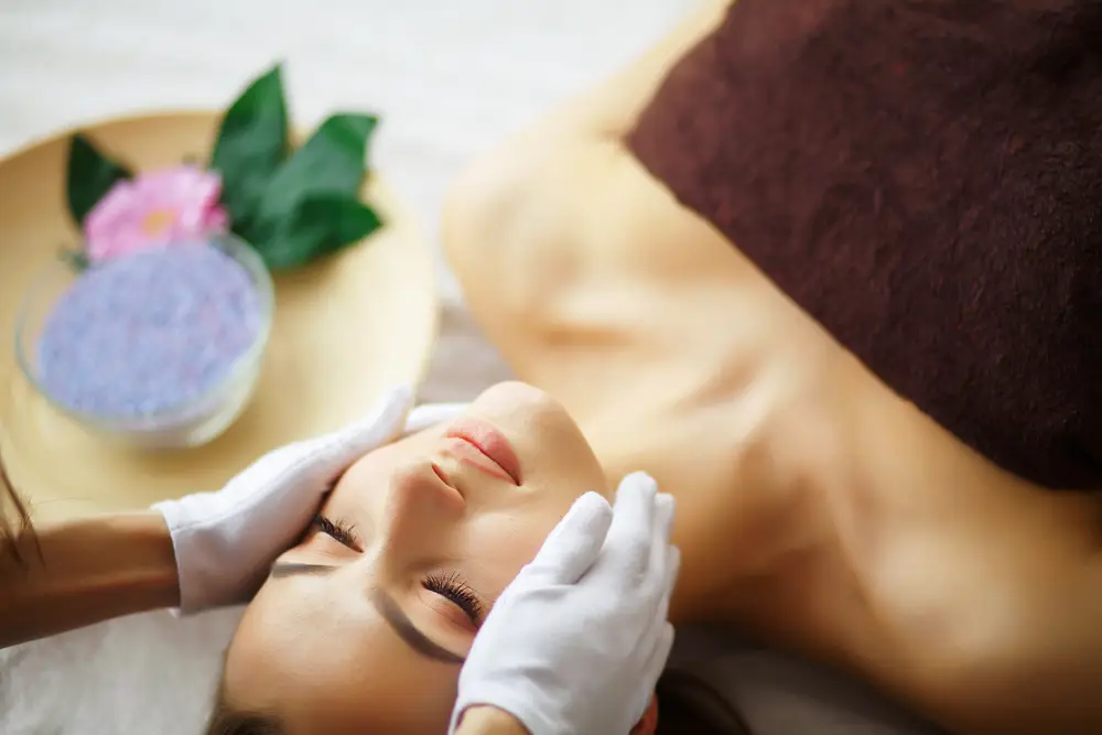 Woman receiving a relaxing Bojin facial treatment on a spa treatment bed with therapist in white gloves