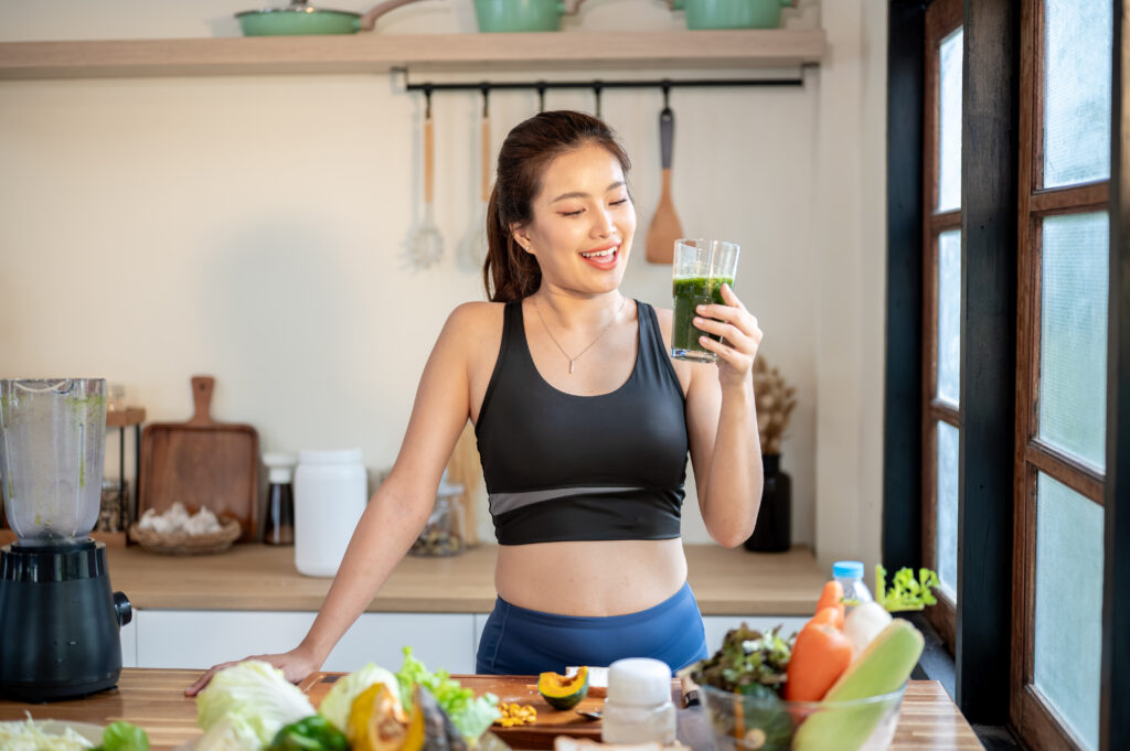 Woman drinking a green smoothie while preparing fresh vegetables to support natural detox and healthy living