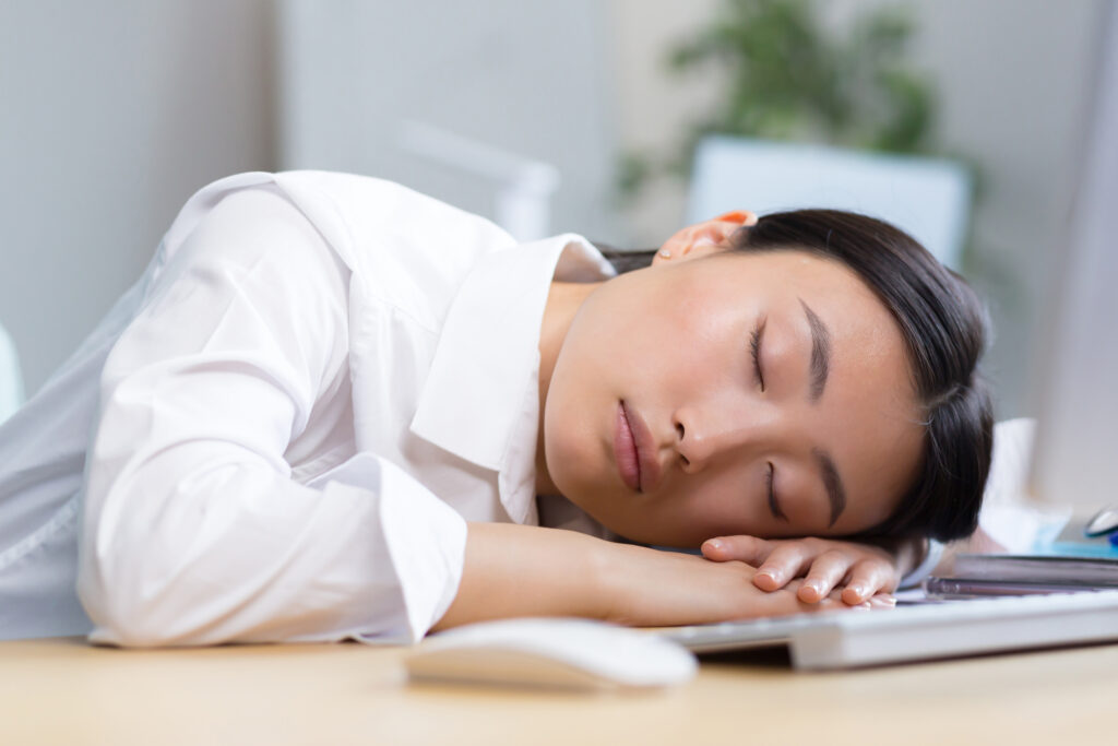 Woman sleeping at her desk, illustrating fatigue and poor sleep as signs the body may need better rest and wellness support